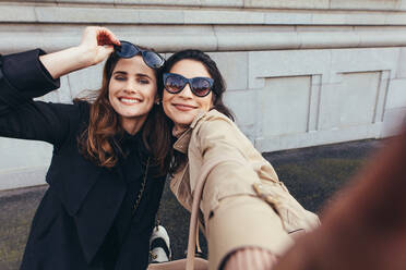 Schöne Freundinnen machen ein Selfie im Freien auf der Straße. Zwei junge Frauen machen ein Selbstporträt draußen in der Stadt und lächeln. - JLPSF01939