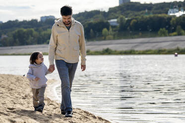 Father and son walking together holding hands by river - ANAF00065