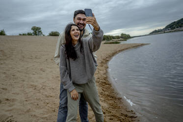Glückliches Paar, das Spaß daran hat, ein Selfie durch ein Smartphone am Fluss zu machen - ANAF00073