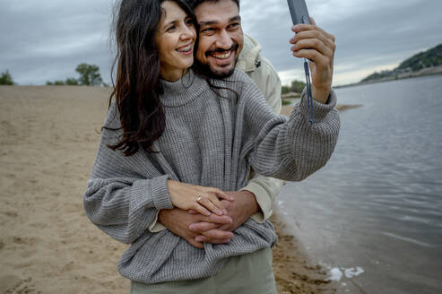 Frau mit Freund nimmt Selfie durch Smartphone am Flussufer - ANAF00074