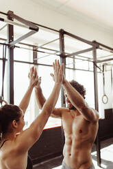 Muscular man and woman giving each other a high five after the training session in gym. Fit couple high five after workout in health club. - JLPSF01949