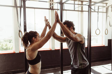 Fit man and woman high fiving at the gym. Fitness couple after successful workout session in cross training gym. - JLPSF01950