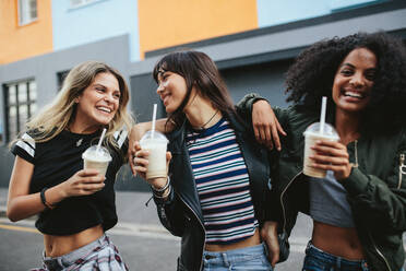 Außenaufnahme von jungen Frauen mit Eiskaffee auf einer Straße in der Stadt. Multirassische Gruppe von Freundinnen beim Eiskaffee. - JLPSF01961
