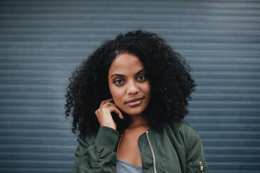 Close up Porträt der schönen jungen Frau mit lockigem Haar. Attraktives afrikanisches amerikanisches weibliches Modell posiert gegen graue Wand. - JLPSF01966