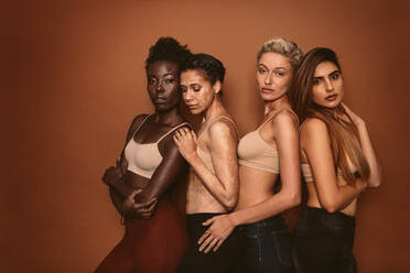 Multi-ethnic group of women wearing bras and jeans against wall