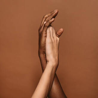 Close up of two female hands together on brown background. Hands of african and caucasian female. - JLPSF02002