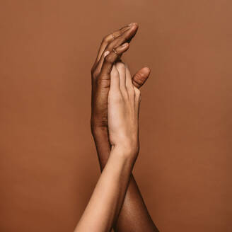 Nahaufnahme von zwei weiblichen Händen auf braunem Hintergrund. Hände einer afrikanischen und einer kaukasischen Frau. - JLPSF02002