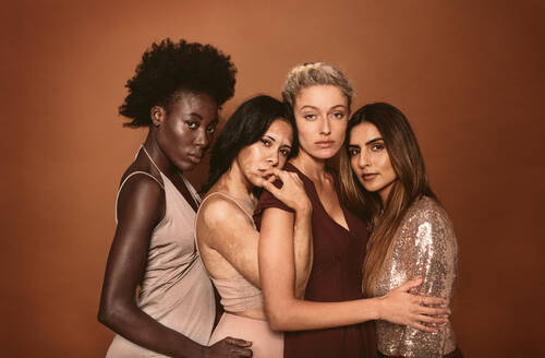 Porträt von stilvollen jungen Frauen, die vor einem braunen Hintergrund stehen. Mehrere ethnische Modemodelle posieren zusammen im Studio. - JLPSF02005