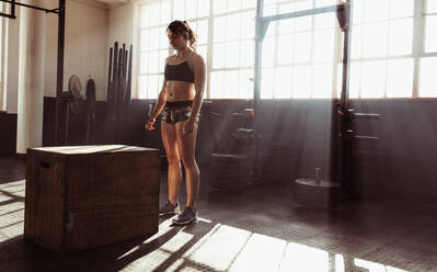 Fokussierte junge Athletin, die bei einem Sprungkasten im Cross-Training steht. Muskulöse junge Frau, die im Fitnessstudio mit einem Kasten trainiert. - JLPSF02012
