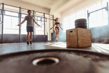 Ein muskulöser Mann und eine Frau trainieren mit Springseilen in einem Cross-Training-Fitnessstudio. Ein junges Paar springt im Rahmen ihres Trainings im Fitnessstudio Seil. - JLPSF02018