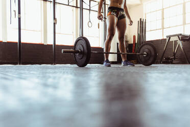 Fit woman with barbell in gym. Female athlete working out with heavy weights at cross training gym. Low angle shot with focus on feet. - JLPSF02031