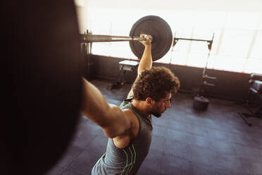 Ein muskulöser Mann trainiert mit einer Langhantel. Ein fitter junger Mann trainiert mit schweren Gewichten im Cross-Training-Fitnessstudio. - JLPSF02039