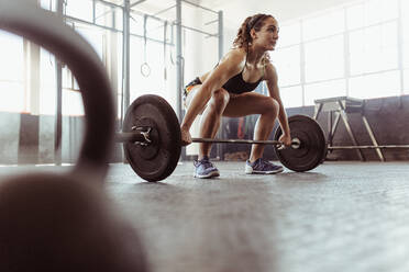 Young woman lifting a barbell at the gym. Fit female athlete exercising with heavy weights at cross training gym. - JLPSF02045