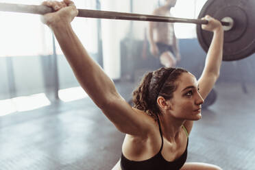 Female performing deadlift exercise with weight bar. Fit young woman doing weight lifting workout at gym. - JLPSF02046