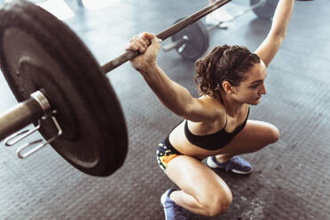 Fit female athlete exercising with heavy weights at cross training gym. Young woman doing deadlift with heavy barbells in gym. - JLPSF02047