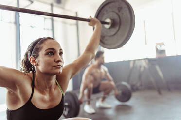 Tough young woman exercising with barbell. Determined female athlete lifting heavy weights at cross training gym. - JLPSF02048