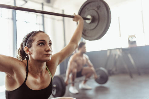 Kräftige junge Frau, die mit einer Langhantel trainiert. Entschlossene Sportlerin, die im Fitnessstudio schwere Gewichte hebt. - JLPSF02048