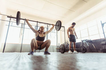 Woman performing deadlift exercise with weight bar. Fit young female doing weight lifting workout at gym. - JLPSF02049