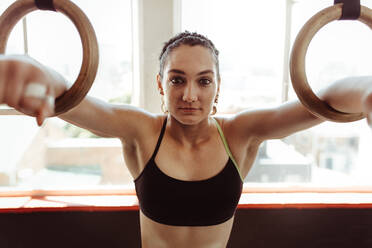 Exercising woman holding gymnast rings and looking away. Female