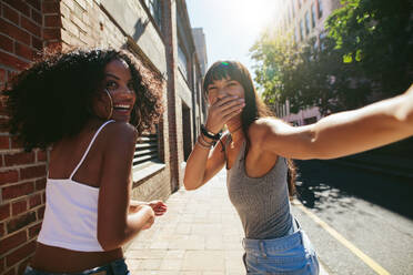 Shot from behind of two young women walking on city street. Female friends walking together outdoors and having fun. - JLPSF02062