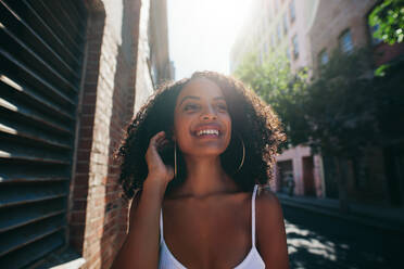 Porträt einer schönen jungen afrikanischen Frau, die die Straße hinuntergeht. Afroamerikanische Frau, die im Freien geht, wegschaut und lächelt - JLPSF02063