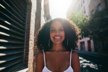 Portrait of smiling young african woman with curly hair on road. Afro american female standing outdoors and looking at camera. - JLPSF02064