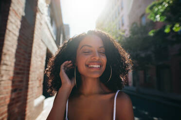 Close up Porträt der schönen jungen afrikanischen Frau zu Fuß im Freien in der Stadt mit ihren Augen geschlossen. Afro-amerikanische Frau zu Fuß im Freien und lächelnd. - JLPSF02065