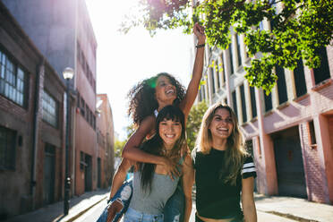 Drei glückliche junge Frauen, die sich auf der Straße amüsieren und lächeln. Gruppe multiethnischer Freunde, die sich auf der Straße amüsieren. - JLPSF02073