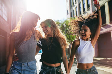 Außenaufnahme von drei jungen Frauen, die lächelnd auf einer Straße in der Stadt spazieren gehen. Gruppe von Freunden, die sich auf einer Straße in der Stadt vergnügen. - JLPSF02075