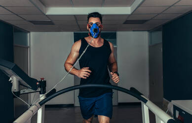 Portrait of runner wearing mask on treadmill in sports science laboratory. Sports man running on treadmill and monitoring his fitness performance. - JLPSF02083