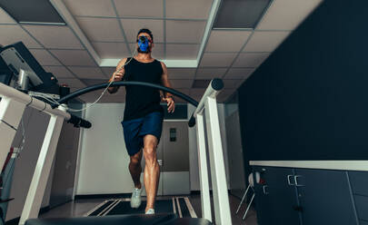 Männlicher Athlet mit Maske, der auf dem Laufband läuft, um seine Fitnessleistung zu analysieren. Läufer, der seine Leistung im sportwissenschaftlichen Labor testet. - JLPSF02085
