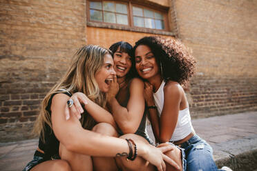 Drei schöne und glückliche Mädchen, die an einer Straße in der Stadt sitzen. Junge Leute, die sich ausruhen und Spaß im Freien haben. - JLPSF02088