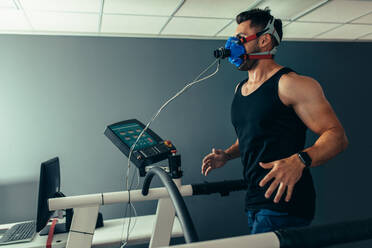 Fitness man running on treadmill with a mask testing his performance. Athlete examining his performance in sports science lab. - JLPSF02090