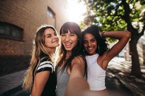 Außenaufnahme von drei jungen Frauen, die sich auf der Straße amüsieren und ein Selfie machen. Multirassische Freundinnen, die einen Tag in der Stadt genießen. - JLPSF02102