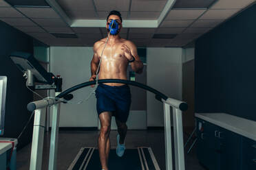 Fit young man running on treadmill with a mask in sports lab. Athlete examining his performance in sports science lab. - JLPSF02104