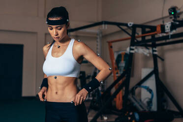 Fitte junge Frau mit Motion-Capture-Sensoren an ihrem Körper im Sportlabor. Eine Sportlerin testet ihre Leistung im Biomechanik-Labor. - JLPSF02109