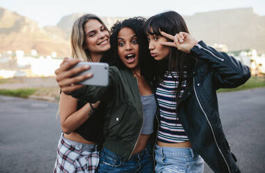 Glückliche Freundinnen machen ein Selfie mit einem Smartphone. Eine multiethnische Gruppe von Frauen hängt in der Stadt ab und macht ein Selbstporträt mit einem Mobiltelefon. - JLPSF02135