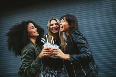 Lächelnde drei junge Frauen mit Eiskaffee auf der Straße in der Stadt. Multiethnische Gruppe von Freundinnen, die zusammen Eiskaffee trinken. - JLPSF02146