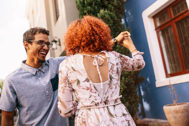 Glückliches Paar tanzt und hat Spaß vor ihrem Haus. Lächelnder Mann hält die Hand seiner Partnerin beim Tanzen. - JLPSF02150