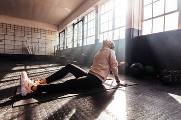 Frau macht Dehnungsübungen auf einer Matte sitzend im Fitnessstudio. Frau wärmt sich für das Training im Fitnessstudio auf. - JLPSF02158