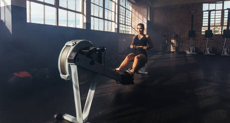 Sportliche junge Frau, die an einem Trainingsgerät im Fitnessstudio trainiert. Frau stärkt ihre Muskeln durch das Ziehen von Gewichten im Fitnessstudio. - JLPSF02165