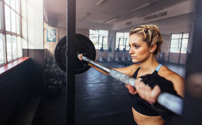 Weibliche Athletin macht Übung mit Hantelstange im Fitnessstudio. Frau trainiert mit Gewichten im Fitnessstudio. - JLPSF02175