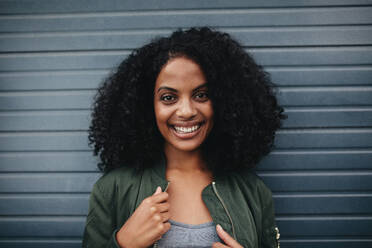 Close up Porträt einer lächelnden afrikanischen Frau, die vor einem grauen Hintergrund steht. Afroamerikanische Frau schaut in die Kamera. - JLPSF02192