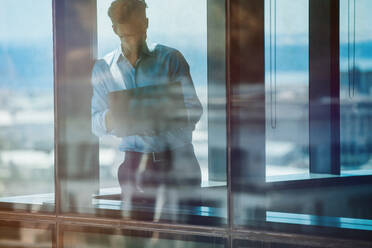 Mature businessman standing by window and using laptop. Entrepreneur standing inside office building and working on laptop computer. - JLPSF02199