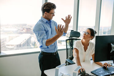 Ein reifer Mann erklärt einer asiatischen Kollegin, die an ihrem Schreibtisch sitzt, eine neue Geschäftsstrategie. Zwei Geschäftsleute arbeiten zusammen im Büro. - JLPSF02205