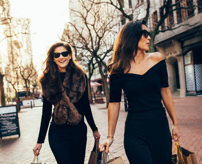 Zwei befreundete Frauen mit Einkaufstüten auf der Straße in der Stadt. Weibliche Käufer im Freien auf der Straße mit Papiertüten. - JLPSF02210
