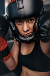 Close up portrait of a female boxer in her boxing gear. Woman boxer at a boxing studio wearing head guard and boxing gloves. - JLPSF02216