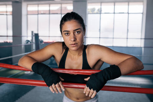 Eine weibliche Boxerin steht in einem Boxring und stützt ihre Arme auf das Seil des Boxrings. - JLPSF02218