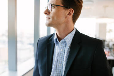 Cropped shot of mature businessman standing in office. Caucasian male executive in suit and eyeglasses looking away and thinking. - JLPSF02235