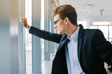 Seitenansicht eines reifen Geschäftsmannes, der in einem Büro steht. Eine kaukasische männliche Führungskraft steht am Fenster und schaut nach draußen. - JLPSF02239